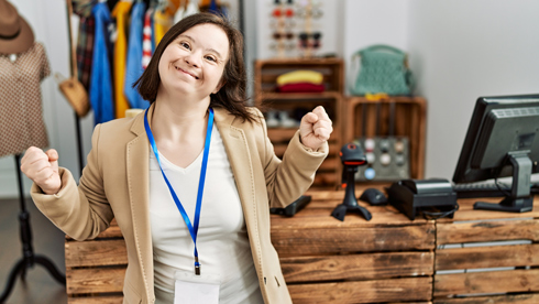 young down syndrome woman working in retail boutique, very happy and excited doing winner gesture with arms raised, smiling