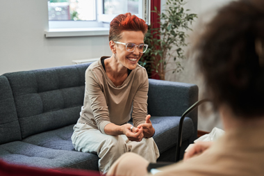 woman laughing and smiling whilst sitting on sofa and talking during therapy