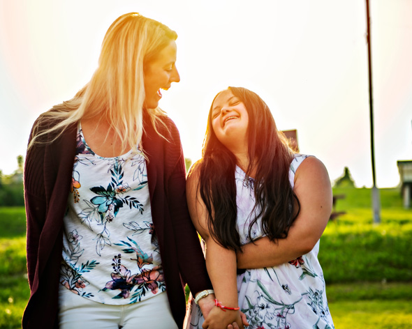 a portrait of down syndrome adult girl smiling outside at sunset with family friend, carer